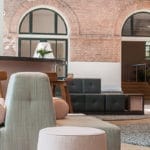 Moderner Loungebereich mit verschiedenen Sitzmöglichkeiten, darunter Barhocker und Sofas, vor Backsteinbögen und großen runden Fenstern, komplett mit einem Bierlagerschrank (450 Liter, Höhe 180 cm).