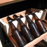 Fünf braune Bierflaschen in einer Holzkiste, von oben bei hellem Licht gesehen.