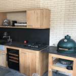 Outdoor kitchen with wooden cabinets, a black countertop, a built-in gas stove and a wine cooler (40 bottles, multiple zones, 84cm height) grill.