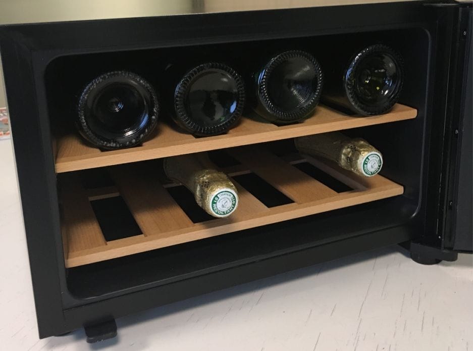 Een kleine Champagne-bewaarkast (25 liter) met drie planken met elk horizontaal geplaatste wijnflessen. de Champagne-bewaarkast heeft een zwarte buitenkant en houten rekken.