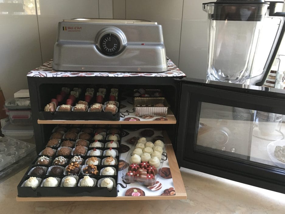 A countertop containing a series of Chocolate climate cabinet (25 liters) in a box, with a toaster oven and a blender in the background.