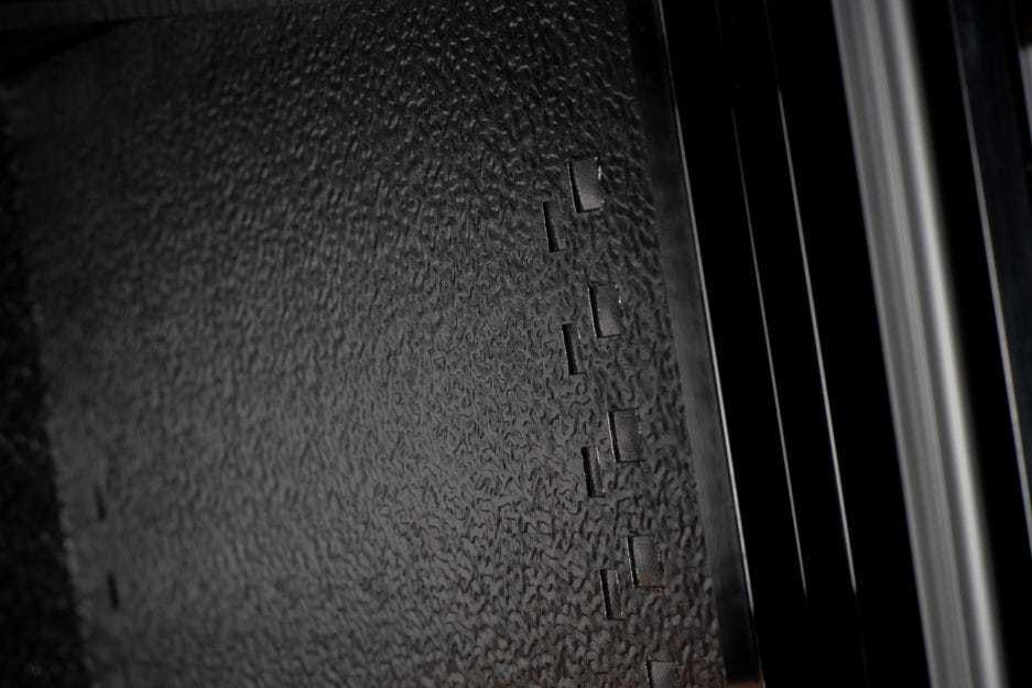 Close-up of a textured black surface with embossed letters, with a blurred background of the Wine Climate Cabinet (40 bottles, multiple zones, 84 cm height).
