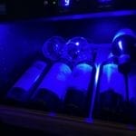 Cave à vin et verres rangés dans une cave à vin éclairée avec éclairage bleu, affichage des températures sur panneaux numériques.