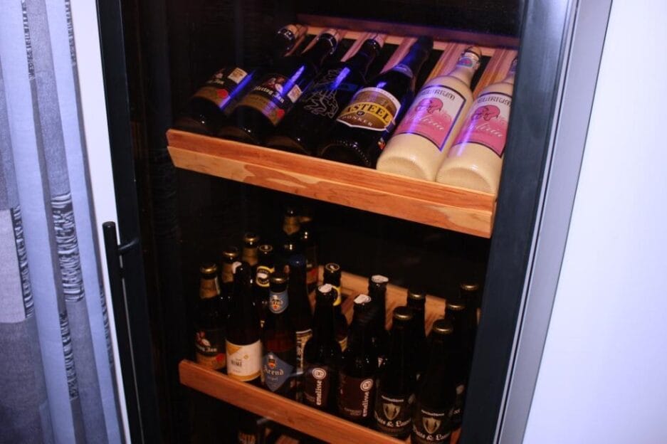 Verlichte bierkast gevuld met diverse flesjes bier op houten de houten plateaus.