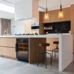 Modern kitchen with wooden cabinets, island with stools, hanging lamps and a wine cooler (40 bottles, multiple zones, 84 cm height) with a view of the garden through large sliding doors.