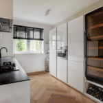 Moderne Kücheneinrichtung mit schwarzer Arbeitsplatte, weißen Schränken, einem Weinschrank (200 Flaschen, eine Zone, 180 cm Höhe und einem Fenster).