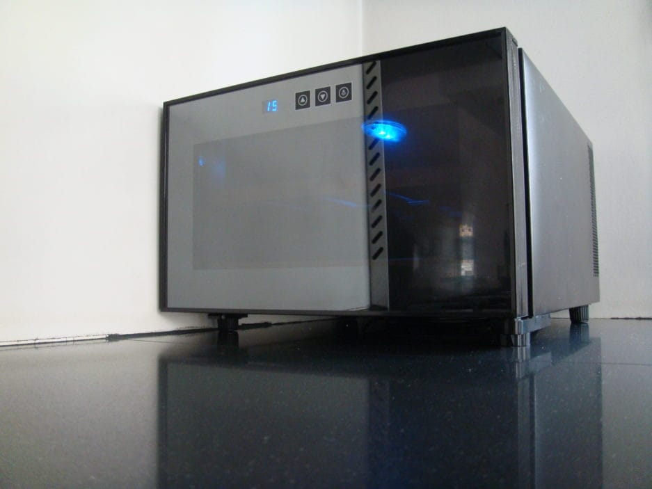 Ein moderner Käse-Klimaschrank (25 Liter + zwei Käsebretter) mit Digitalanzeige mit der Uhrzeit „15“ und blauem Licht, steht auf einer Küchenarbeitsplatte.