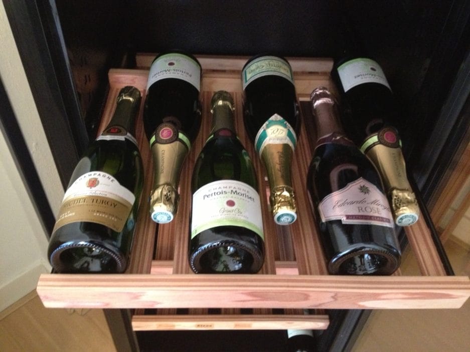 A Champagne storage cabinet containing six bottles of various brands of champagne, neatly arranged in a homely setting.