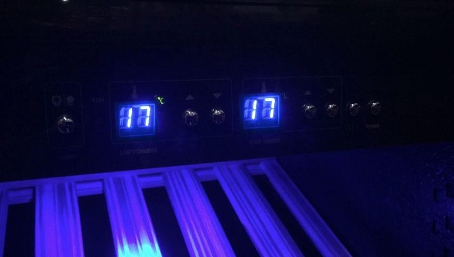 Bedienfeld eines Schokoladenlagerschranks (Höhe 164 cm, 275 Liter für Schokolade) mit digitalen Displays mit der Anzeige 17, beleuchtet durch blaue Hintergrundbeleuchtung, und verschiedenen Tasten und Symbolen, darunter ein Ventilator und ein Wassertropfensymbol.