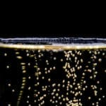 Een close-up van een Champagne-bewaarkast (25 liter) met bubbels die naar de oppervlakte stijgen tegen een zwarte achtergrond.