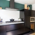 Modern kitchen with black cabinets, a gas stove, built-in oven and a white geometric back wall, accented with a storage shelf wall and decorative items.