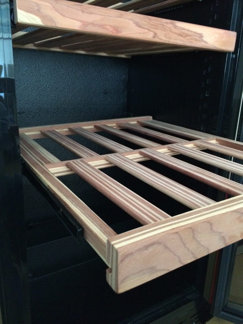 Storage shelf spice rack drawer partially extended from a black shelf, showing off the slatted design.