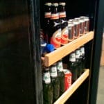 Eine Vielzahl von Flaschen und Dosen aus dem Storage Shelf, ordentlich angeordnet auf Holzregalen in einem schwarzen Kühlschrank.