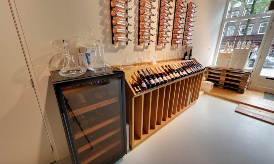 Interieur van een wijnwinkel met links een wijnbewaarkast, met diverse wijnflessen en karaffen op de bewaarkast erboven.