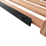 L-förmige Metallhalterung, befestigt an Holzlatten, vor schwarzem Hintergrund mit einer gerändelten Aussparung am unteren Bildrand. Kugelgelagertes Geländersystem