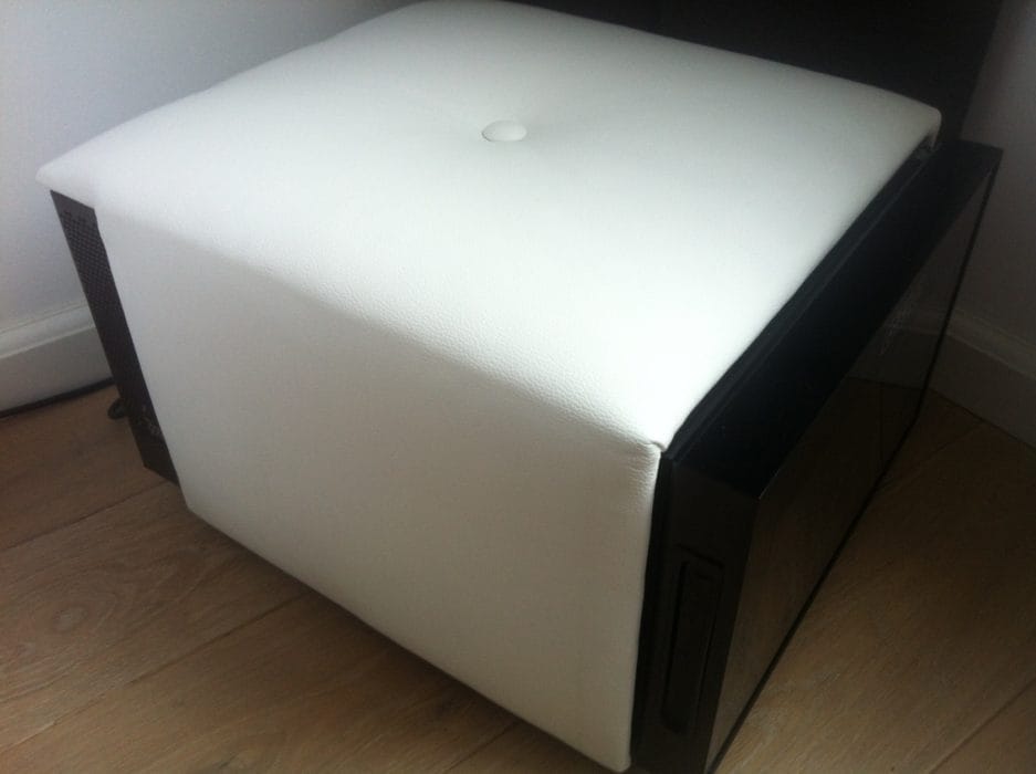 Un cuir blanc avec un dessus matelassé et des boutons, placé à côté d'un haut-parleur noir sur un plancher en bois.