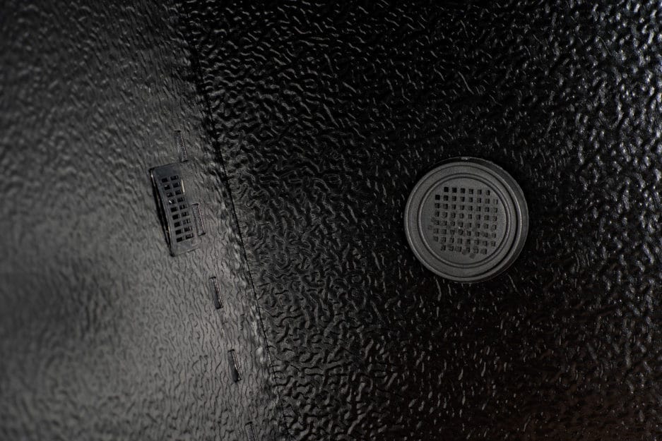 Close-up of a black textured surface with a circular speaker grille and two slim rectangular vents.