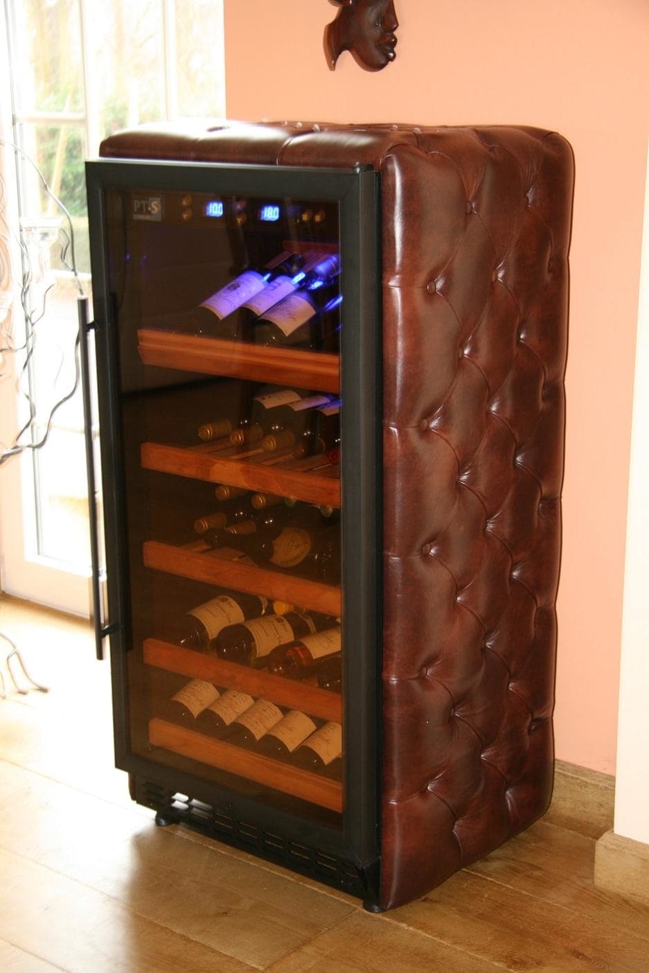 A Leather wrapped in brown leather with a quilted pattern, with an open glass door showing several shelves filled with wine bottles.