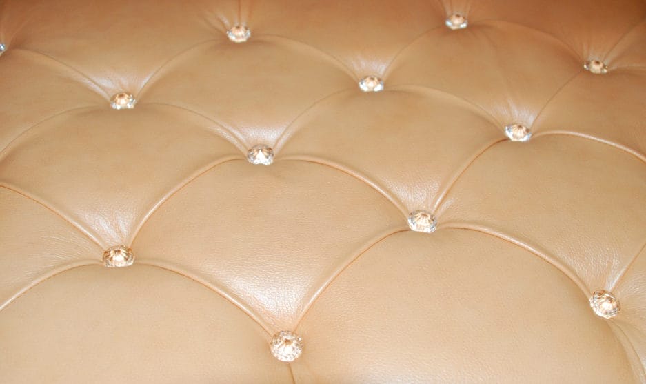 Close-up of a leather tufted upholstery with diamond-shaped patterns and crystal buttons.