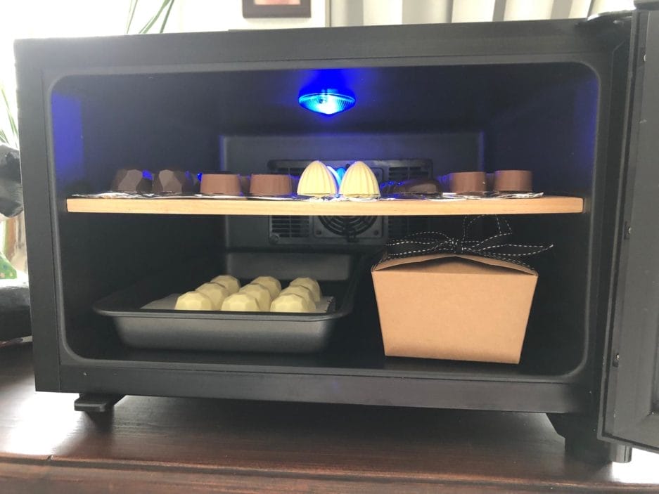 A 3D printer housing with blue light, which prints multiple small, white spherical objects on the platform.