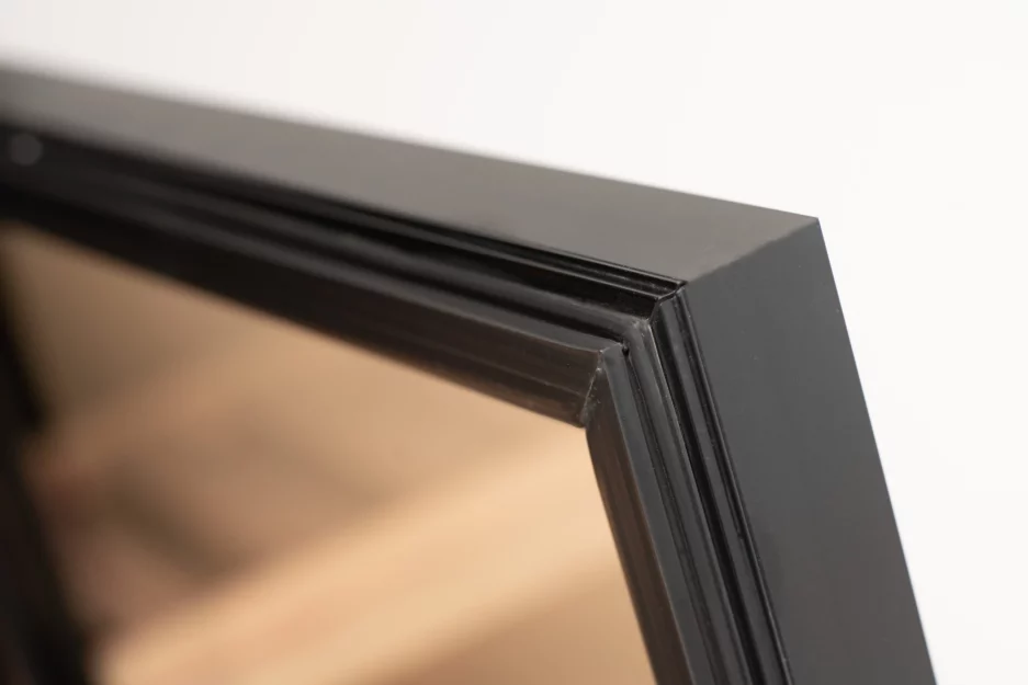 Close-up of the corner of a black picture frame against a white background, showing details of the frame and glass edge.