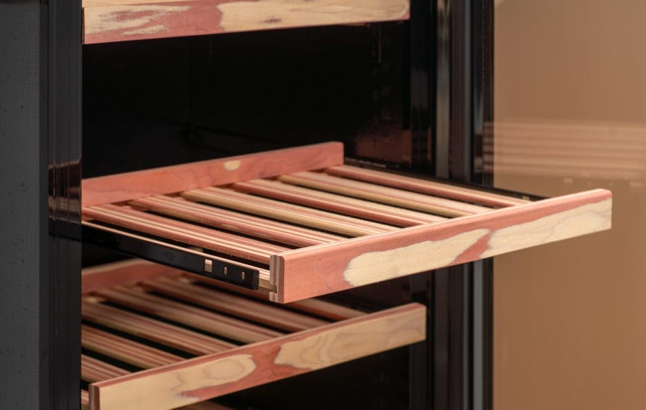 A close-up of an open, wooden cigar humidor drawer, showing the construction and empty slots.
