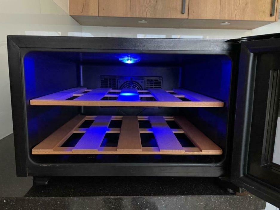 Ein Weinkühlschrank mit Holzregalen, beleuchtet von blauem Licht, eingebaut in dunkle Küchenschränke.