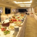 Salle de banquet spacieuse avec un buffet de plats et de salades variés, comprenant des stations de boissons et de desserts, décorée d'images florales sur les murs.