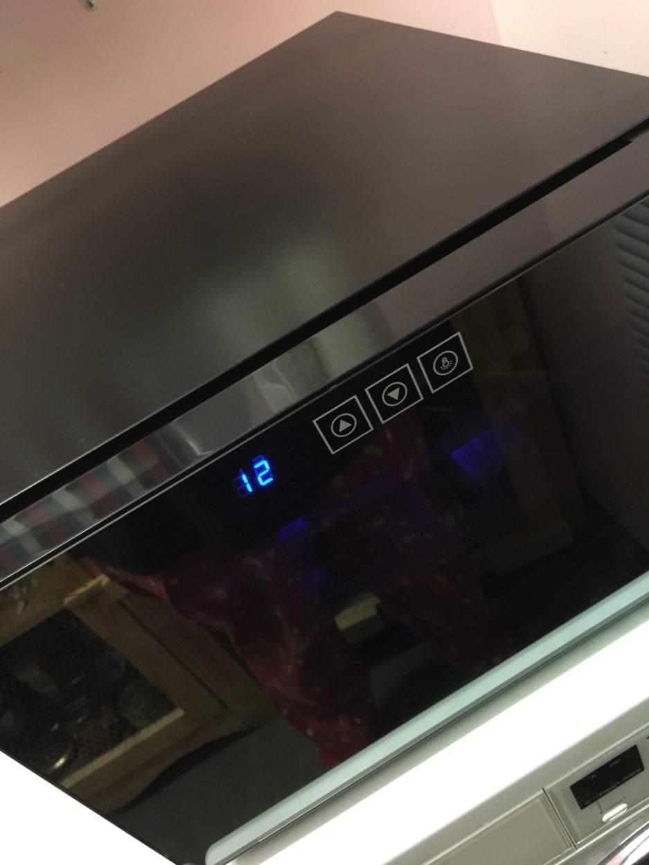 Modern black microwave oven with a digital clock showing the time as 12, seen in a kitchen setting with a reflection of a person on the glass.
