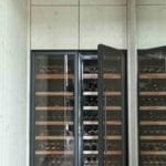 Zwei große, vertikal ausgerichtete Weinkühlschränke, eingebaut in eine helle Holzwand, mit jeweils mehreren Regalen gefüllt mit verschiedenen Weinflaschen.