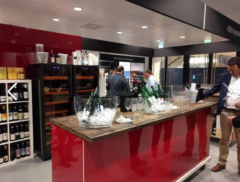 People gather at a wine tasting, with several bottles of wine on display and participants chatting in a bar.