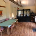 Salle à manger spacieuse avec une grande table verte, des chaises en bois et un meuble noir avec poutres apparentes et parquet.