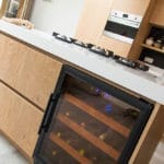Moderne Küche mit hellen Holzschränken, einem Weinkühler und einem Gasherd auf einer weißen Arbeitsplatte.