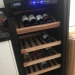A wine cooler open, containing several bottles of wine on wooden racks, with a digital temperature display on top.