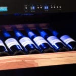 Horizontal gelagerte Weinflaschen in einem modernen Weinkühler mit Holzregalen und digitaler Temperaturanzeige.