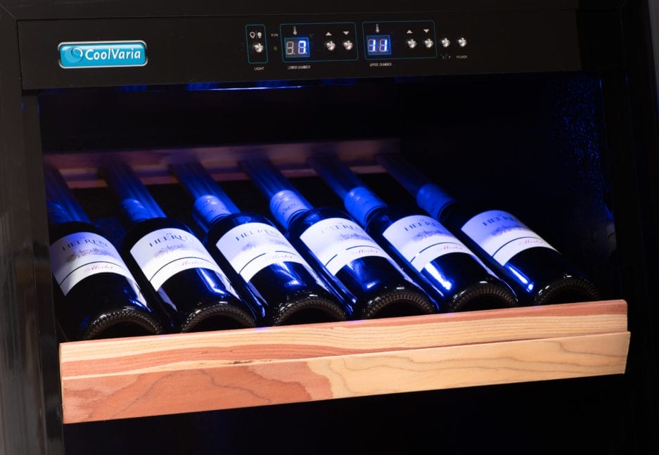 Wine bottles stored horizontally in a modern wine cooler with wooden shelves and a digital temperature display.