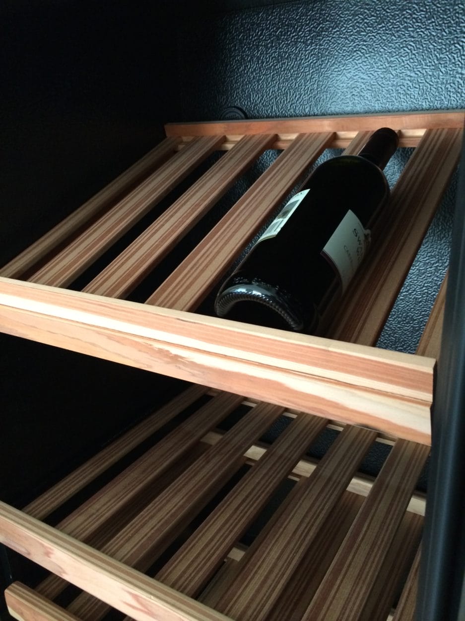 A single bottle of wine lying horizontally on a wooden rack in a dark storage room.