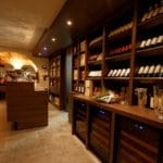 Een gezellig wijnwinkelinterieur met houten planken gevuld met verschillende wijnflessen en een centrale proefbalie.