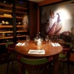 Une table ronde pour quatre personnes dans un restaurant chaleureux avec une fresque représentant un paon au mur et des bouteilles de vin sur des étagères.