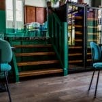 Intérieur d'un bar élégant avec des chaises bleu sarcelle, des marches en bois vert et une cave à vin éclairée, alliant une atmosphère contemporaine et cosy.