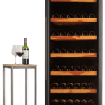 Réfrigérateur à vin noir haut rempli de plusieurs casiers de bouteilles de vin, à côté d'une table avec une bouteille de vin et deux verres.