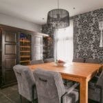 Une salle à manger moderne avec une table en bois, des chaises à rayures, du papier peint à motifs et une cave à vin intégrée.