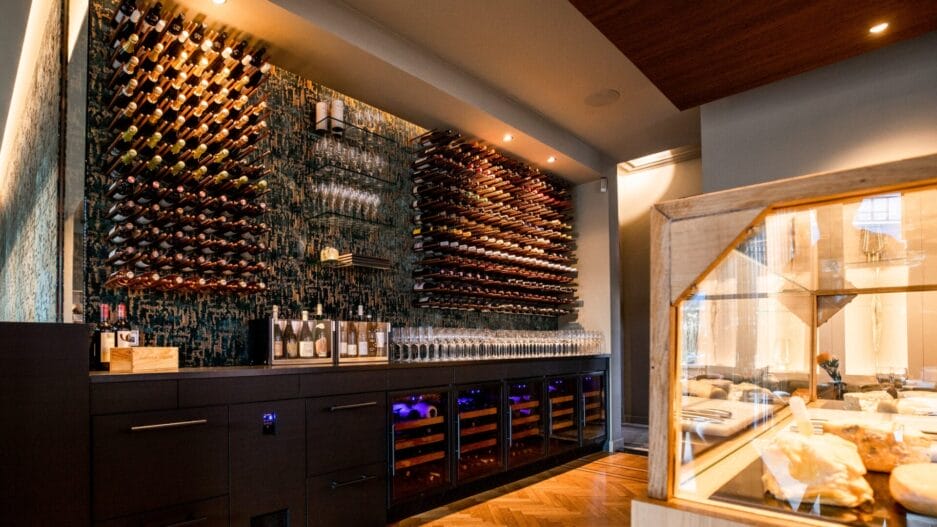 A modern wine cellar with extensive bottle racks on the wall, a glass cheese display case and a stylish, spacious interior.