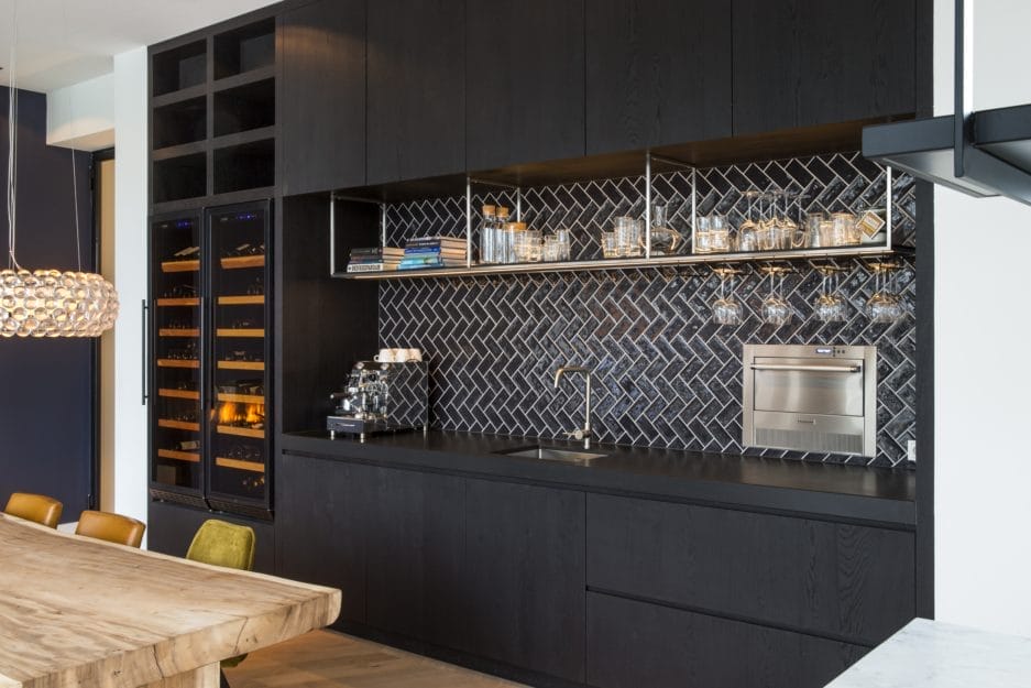 Moderne keuken met zwarte kasten, chevron-achterwand, inbouwapparatuur en een houten eettafel.