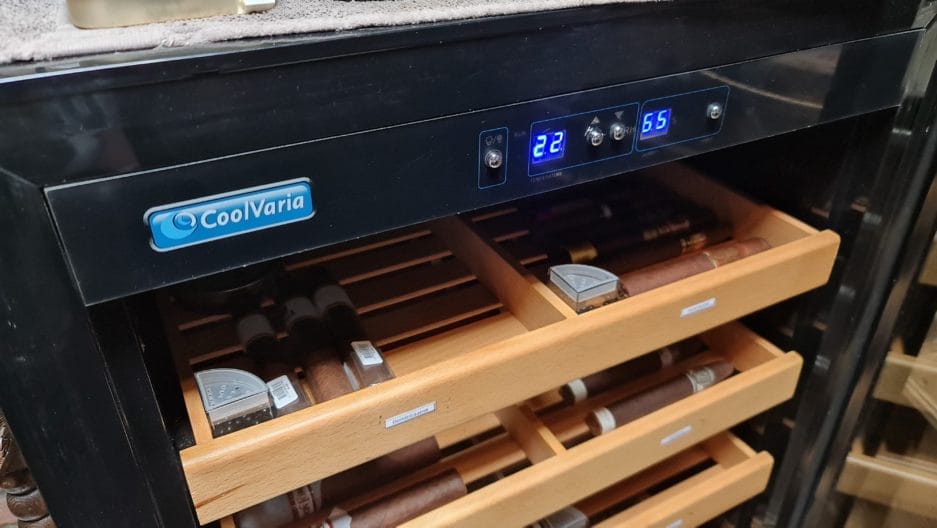 Een wijnkoeler met digitaal temperatuurdisplay van 22 en 65 graden, open lade waar rijen wijnflessen zichtbaar zijn.