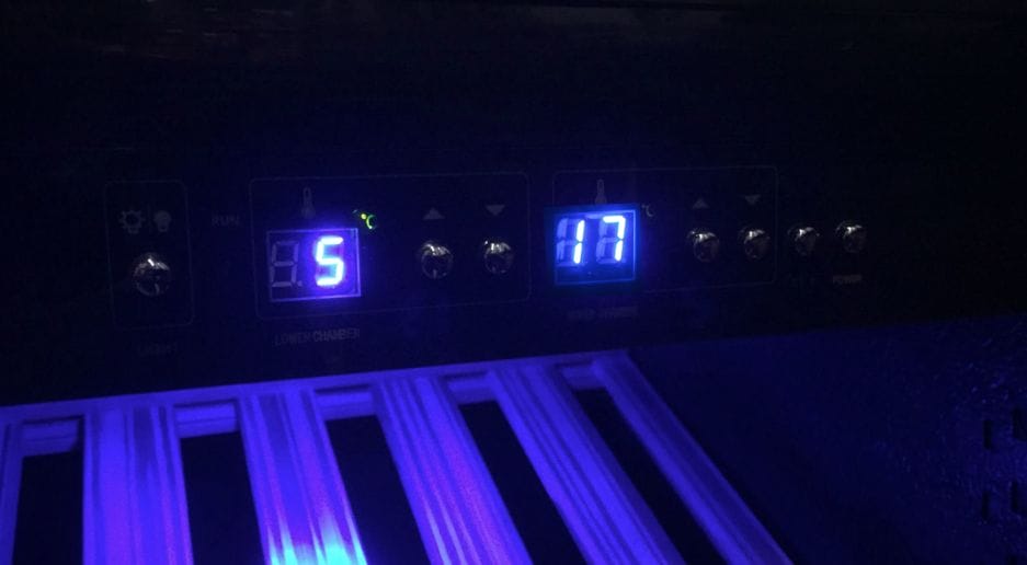 Beer climate cabinet with setting "5" and "11" with illuminated buttons and labels, placed above glowing blue compartments.