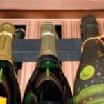 Drei Flaschen Champagner in einer Holzkiste, mit zwei sichtbaren Etiketten mit der Aufschrift „Henriot“ und einer mit farbenfrohen Mustern verziert.