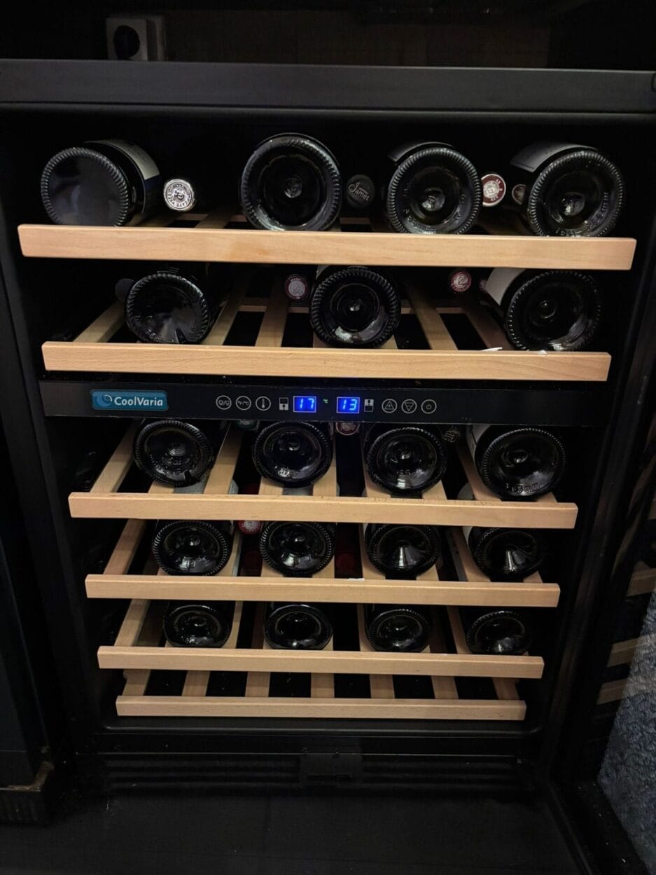 De wijnklimaatkast met houten plateaus en verschillende flessen wijn horizontaal opgeborgen, met het display met digitale temperatuurweergave in het midden.
