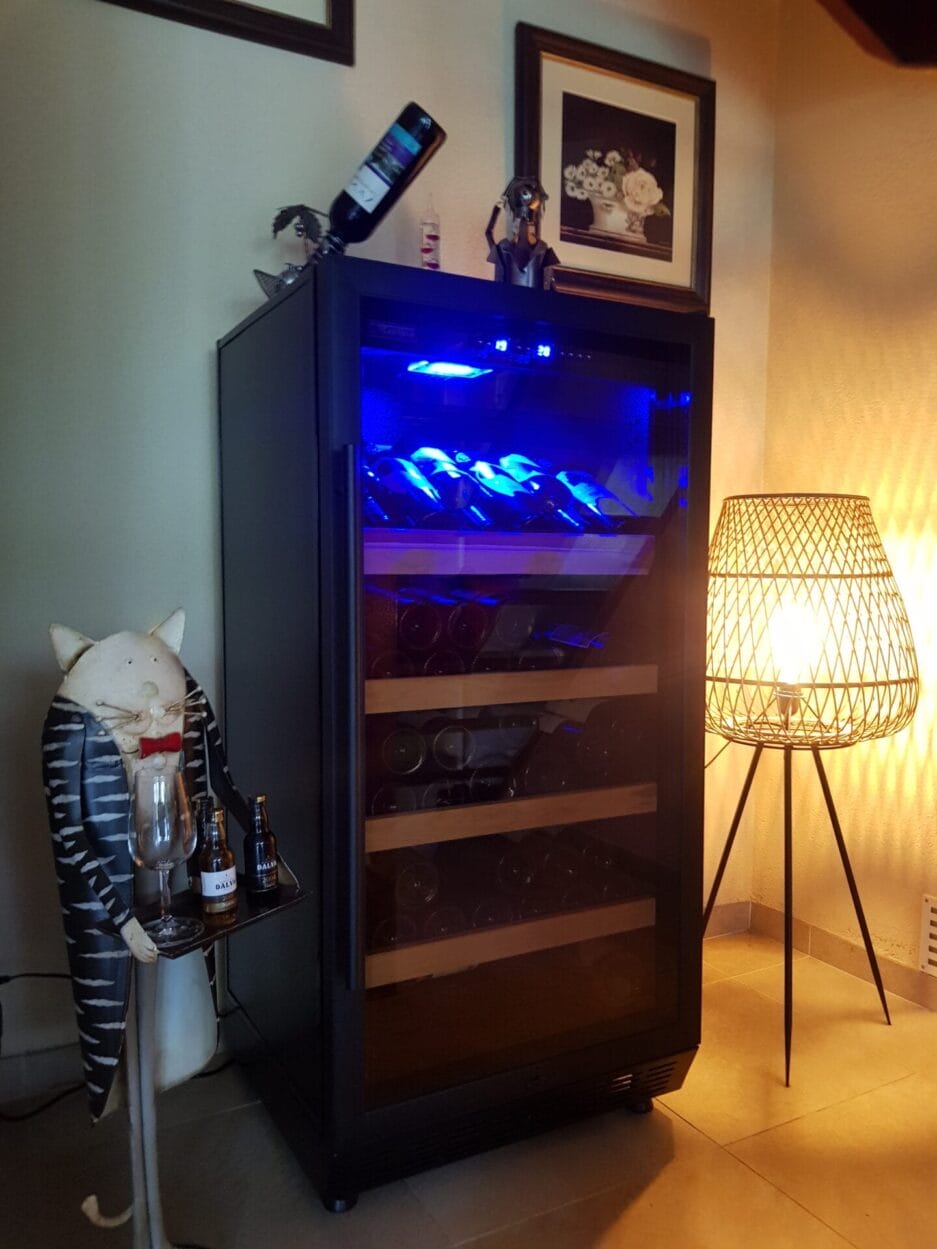 Wijnbewaarkast met blauwe binnenverlichting, gevuld met flessen, met decoratiestukken.