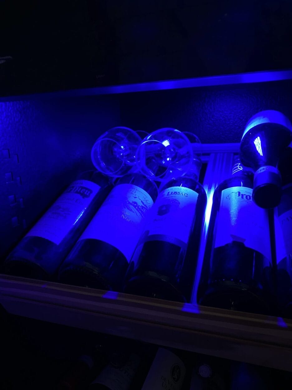 Verschillende wijnflessen en twee wijnglazen (dus meteen op de juiste temperatuur) op een plateau opgeslagen, verlicht door blauw licht.